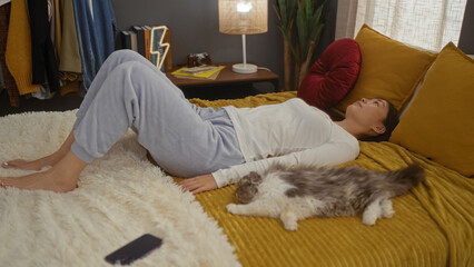 Young chinese woman relaxing on a bed in the bedroom with her pet cat nearby, while cozy indoor surroundings showcase a domestic and homely atmosphere.