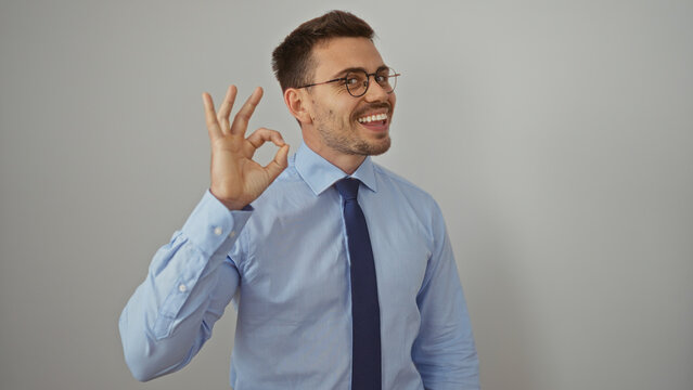 Young hispanic man with a beard and glasses making an ok hand gesture while smiling against an isolated white background.