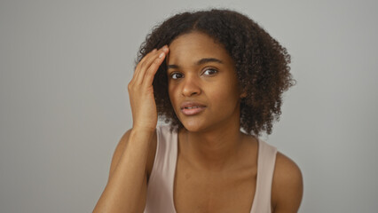 Beautiful young african american woman with curly hair touching her head over isolated white background.