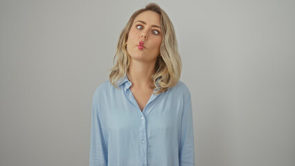 Playful young caucasian woman puckering lips in blue shirt against isolated white background.