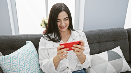 A young woman enjoys her smartphone in a modern living room, showcasing casual style and leisure time.