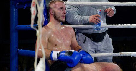 Cornered boxer receives strategic advice from trainer during intense bout.