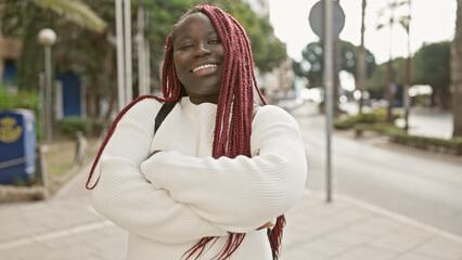 Obraz premium A joyful african woman with red braids posing on an urban street exudes confidence and beauty.