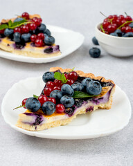 Two pieces of shortbread cake with blueberries and red currants, garnished with a mint leaf.  Seasonal, bright, summer baked goods.