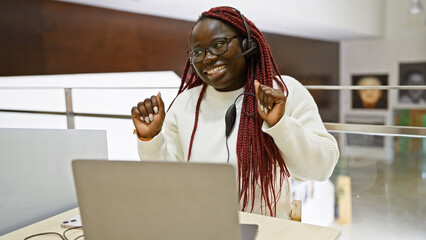 Smiling african woman with braids wearing headset at modern office