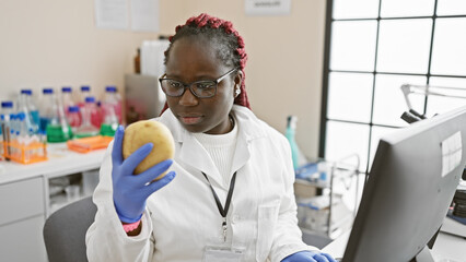 African woman scientist examining a potato in a laboratory with computers, colorful reagents, and medical equipment.