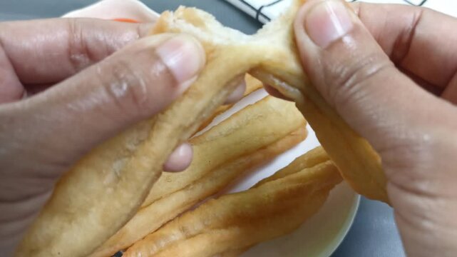 Hand is breaking Cakwe or Cakue or Youtiao. traditional Chinese snack, long golden-brown deep-fried strip of wheat flour dough and very popular in China and Asia. 