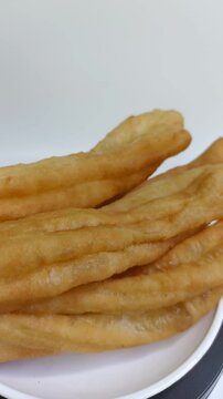 Cakwe or Cakue or Youtiao is traditional Chinese snack, long golden-brown deep-fried strip of wheat flour dough and very popular in China and Asia. Close up, rotating in motion.