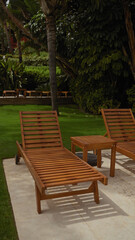 Obraz premium Wooden sun loungers and side table on a lush patio suggest tranquil relaxation and luxury resort living.