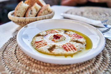 Close-up of hummus garnished with paprika and olive oil, served with bread on a woven placemat at a restaurant.