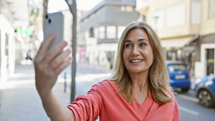 Fototapeta premium Smiling middle-aged caucasian woman taking a selfie outdoors on a city street