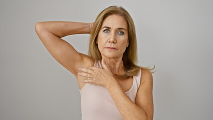Fototapeta premium Mature blonde woman examines underarm against isolated white background, depicting hygiene or health concern.