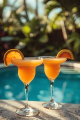 Two orange cocktails by the pool, tropical setting, soft focus background