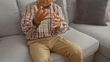 Elderly man engaged in conversation, gesturing with hands while sitting in a cozy living room...