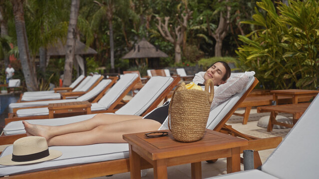 A young woman relaxes on a sunbed at an upscale indonesian resort, embodying tranquility and leisure.