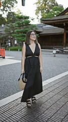 Confidently posing at fushimi inari taisha, a beautiful hispanic woman wearing glasses, smiles broadly, looking around, captivated by the stunning kyoto temple surroundings.