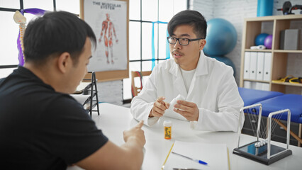 Doctor in lab coat discussing medication with male patient in a clinic's rehabilitation room.