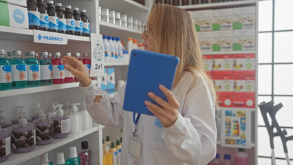 Blonde woman pharmacist in labcoat using tablet in drugstore,