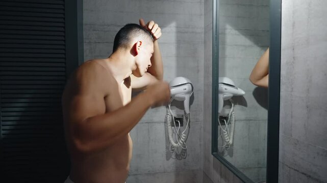 A worried young white man looks at himself in the mirror and inspects his premature receding hairline. Attractive Caucasian male adult in his 20s concerned about losing hair. Male pattern baldness. 