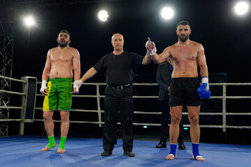Boxing referee declares victorious fighter amidst the aftermath of an intense bout.