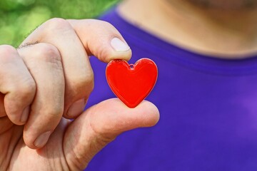 one small red shiny iron beautiful romantic love heart in hand on purple background