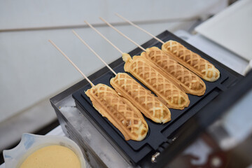 At a food event, a vendor is observed holding waffle sticks freshly prepared on skewers