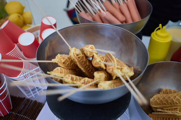 At a food event, a vendor is observed holding waffle sticks freshly prepared on skewers