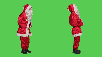 Santa claus character in red suit saying ho ho ho to spread positivity on christmas eve holiday, white beard. Saint nick in costume posing with confidence over full body greenscreen backdrop.