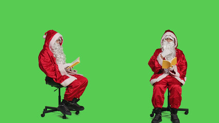 Young man reading poetry book disguised as santa claus in costume sitting on chair, full body greenscreen. Person portraying saint nick enjoying literature or fiction lecture, cultural hobby.