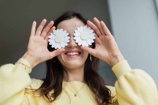 Young woman holding paper flowers over her eyes