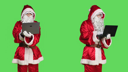 Man in santa costume using laptop to see naughty or nice children list, looking around the globe to send presents on christmas eve. Father christmas concept, person on greenscreen.