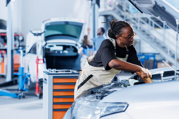 African american woman in car service using professional mechanical tool to repair broken radiator....