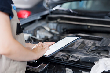 Certified mechanic in garage using tablet to follow checklist while doing maintenance on car. Close...