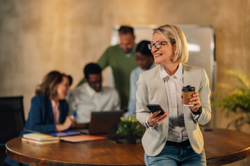 Mature businesswoman using phone on meeting of her interracial team.