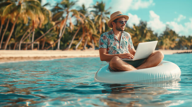Young man in hat and glasses sitting on inflatable circle with laptop in the sea on tronic island background. The concept of freelancing and vacationing. The concept of workaholism