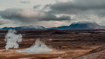 Námafjall Geothermal Area. Tourists in the distance, steaming fumaroles, boiling mud pots. Panorama of suggestive volcanic landscape. Sulfurous springs, solfataras and steam springs.
