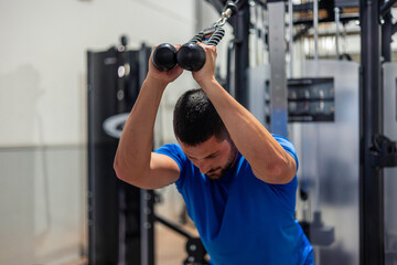 young athlete does triceps exercise with high pulley machine in gym during strength training routine