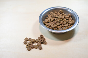Cat food, commercially available dry food made from animal by-products as kibbles in a bowl on a wooden background, copy space, selected focus