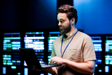 Specialist using laptop to do scans on blade servers in data storage facility. Cloud computing computer service business used for complex calculations and massive datasets processing