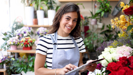 Portrait of a young woman working at the flower shop, using tablet and organizing the business