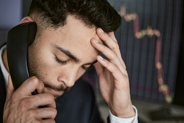 Fototapeta premium Stress, phone call and business man at desk for investment mistake, error or stock market problem in office. Charts, screen and trader with headache for financial crisis, discussion or risk fail