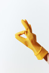 A hand in a yellow rubber glove making an ok sign with thumb and index finger against a white...