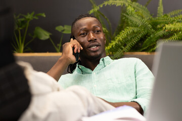 Talking on smartphone, man working on laptop in modern office setting