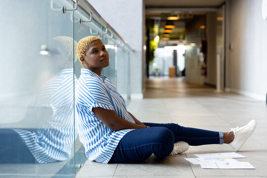Sitting on floor, woman reflecting while looking away, papers scattered around