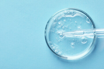 Glass pipette and petri dish with liquid on light blue background, top view. Space for text