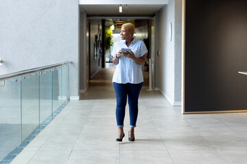 Holding smartphone and looking ahead, african american woman walking in hallway