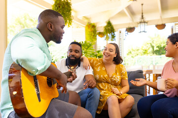 Playing guitar, man entertaining diverse friends while sitting together on cozy patio
