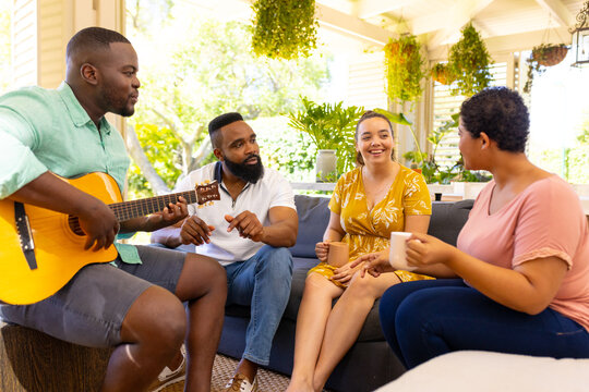 Playing guitar and enjoying coffee, diverse friends relaxing together on patio