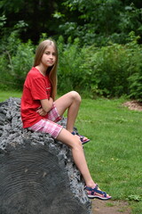blonde girl sitting on a log against the backdrop of a landscape