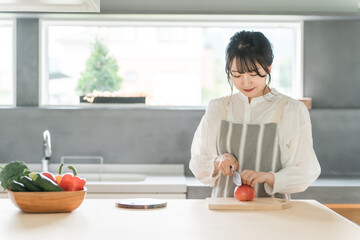 キッチンで料理・家事をする若いアジア人女性・主婦（包丁・切る・野菜・トマト）  © buritora